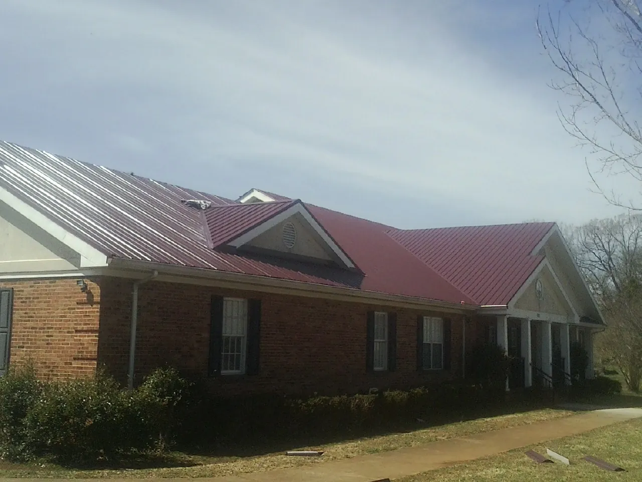 Red metal roof with gabled entries on a long brick building, from a Hail Damage Roof Repair job in Horseshoe Beach