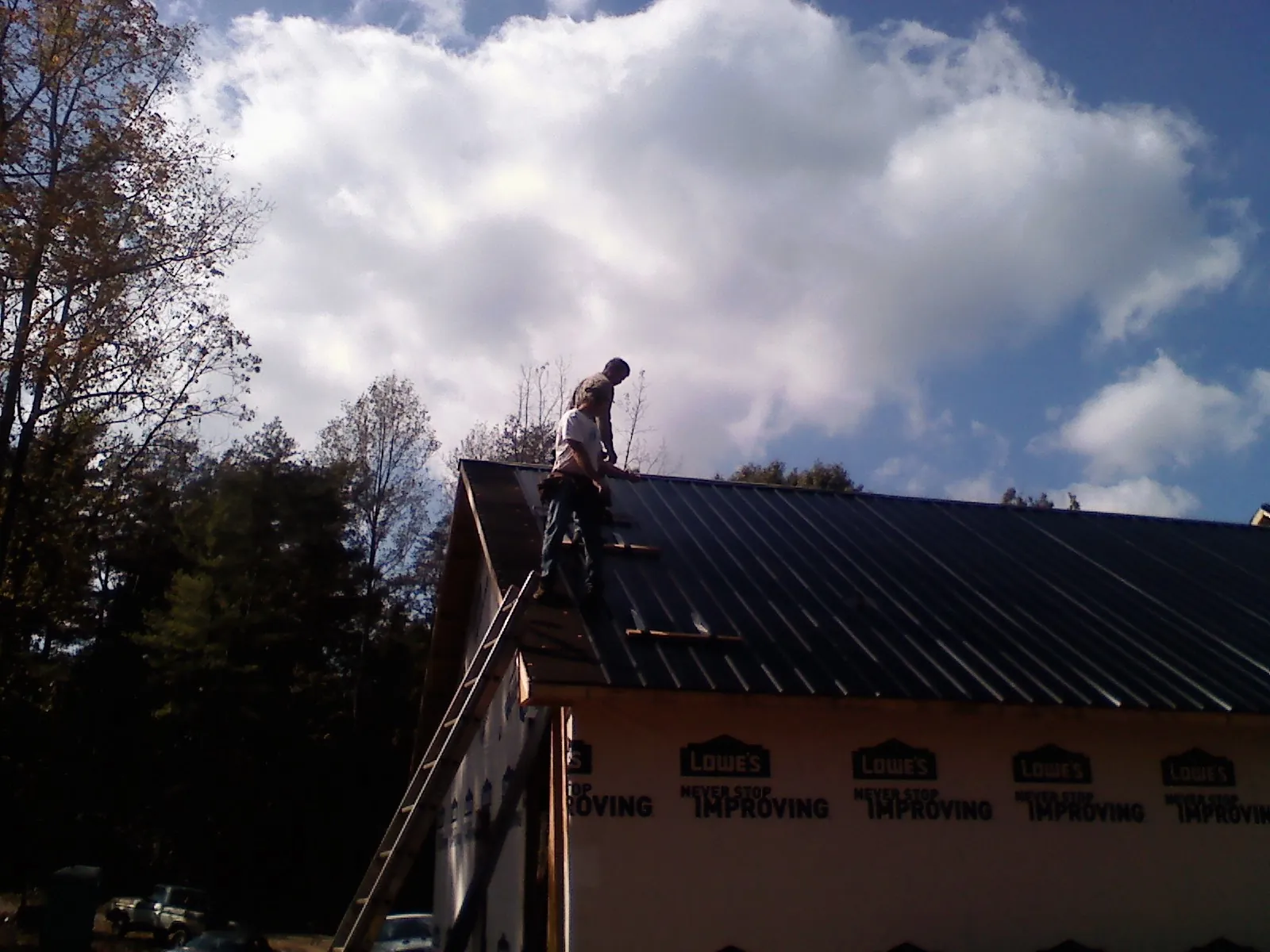 Roofer fastening dark metal panels high against a cloudy sky, from a Roof Inspection job in Horseshoe Beach