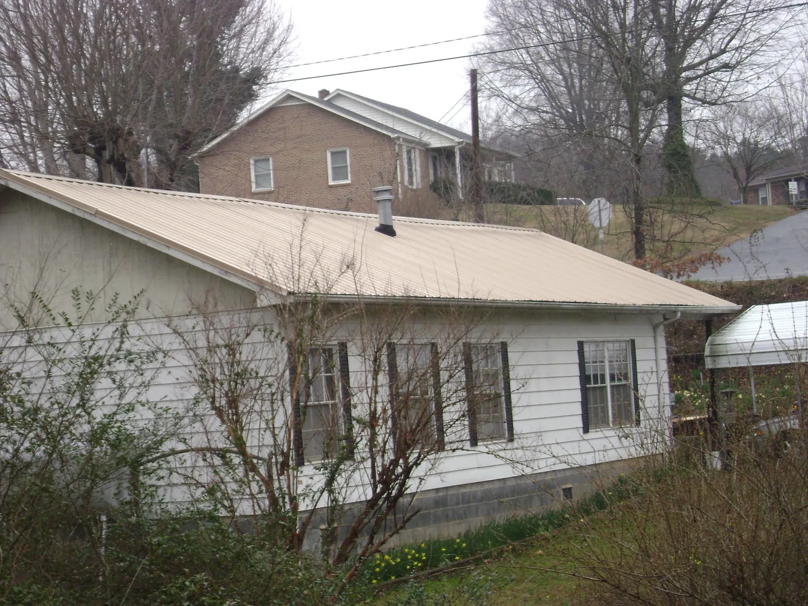 Tan metal roof on a white sided house set into a hillside — Commercial Roofing by Roofing Brothers in Horseshoe Beach