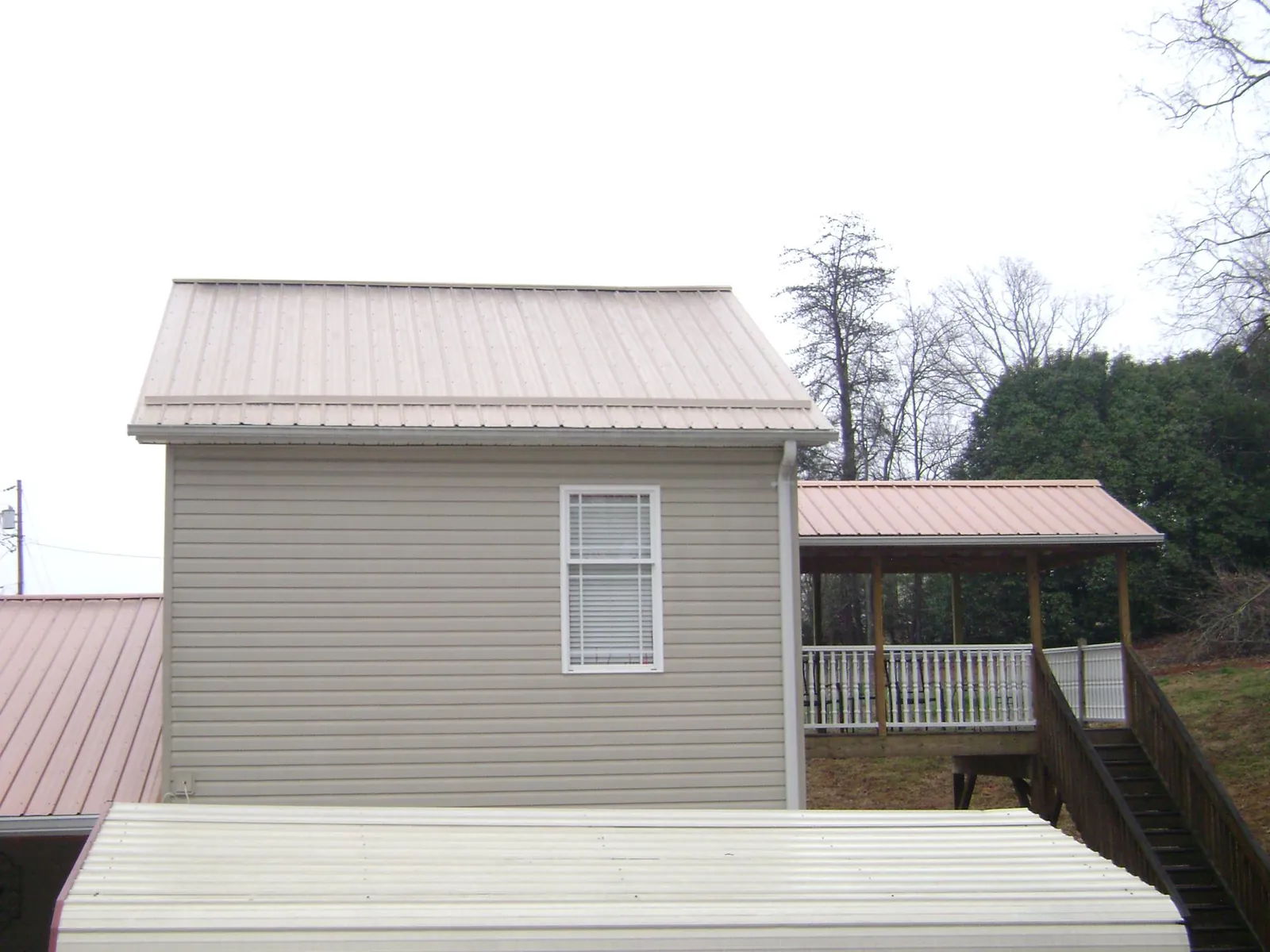 Tan metal roofs on a two story addition and attached porch, from a Roof Replacement job in Horseshoe Beach
